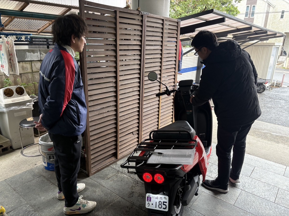 販売店で赤い量産試作車を囲み、操作を確かめる人たち