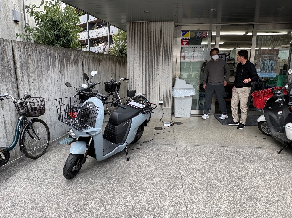 新聞販売店の前に置かれた量産試作車と、話をする人たち